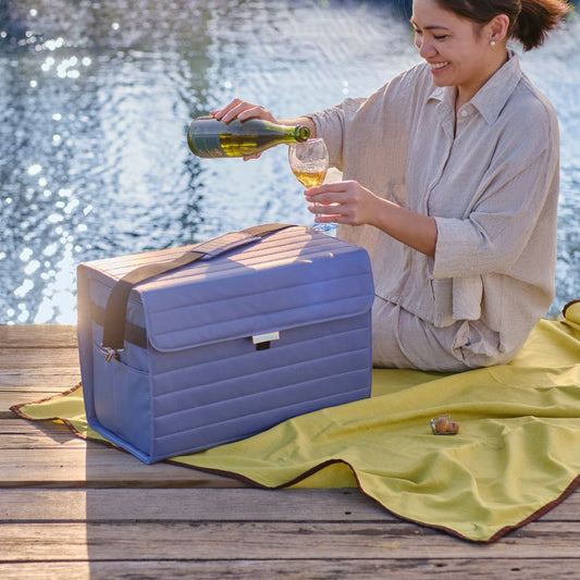 female with a Nutshell soft-sided cooler and a glass of white wine sitting by a lake