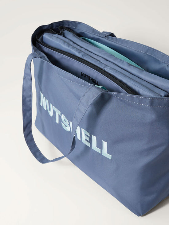 Blue tote bag with 'NUTSHELL' embroidery and folded cooler inside on a light gray background